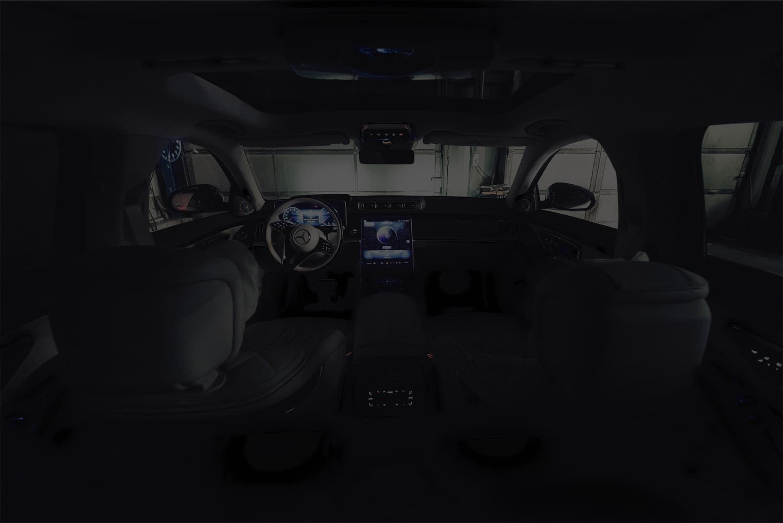 Innenraum einer Mercedes S-Klasse (W223) bei Nacht, vom Fond aus gesehen: Armaturenbrett, Türen, Fußraum und Dachkonsole mit Ambientebeleuchtung